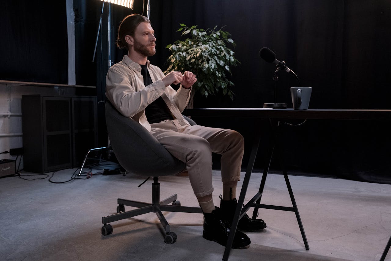 A bearded man sitting in a modern podcast studio with a microphone.